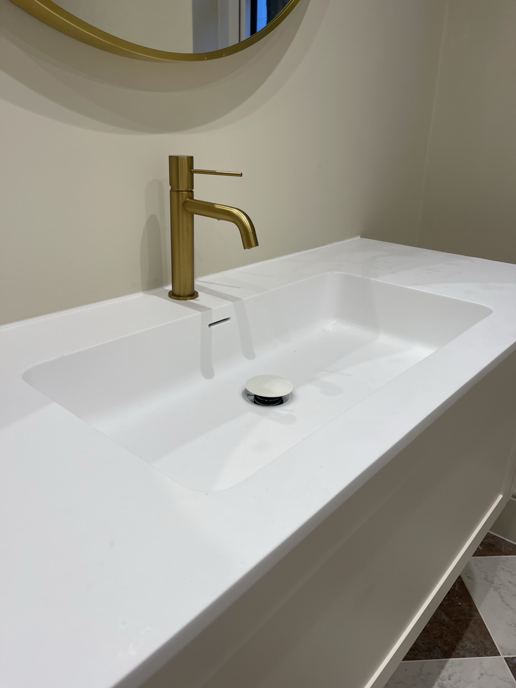 Brushed brass basin mixer tap on a white solid-surface vanity, Shepherd's Bush W12